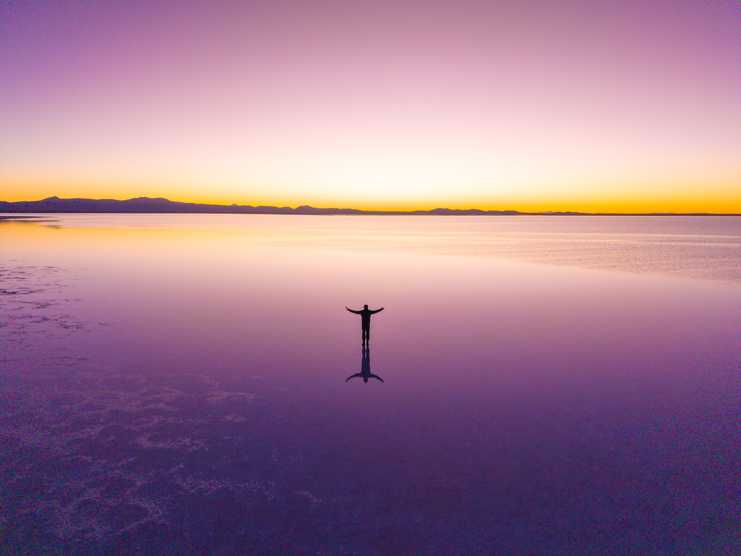 Mike McGovern, arms outstretched on a mirror-still salt flat at sunset